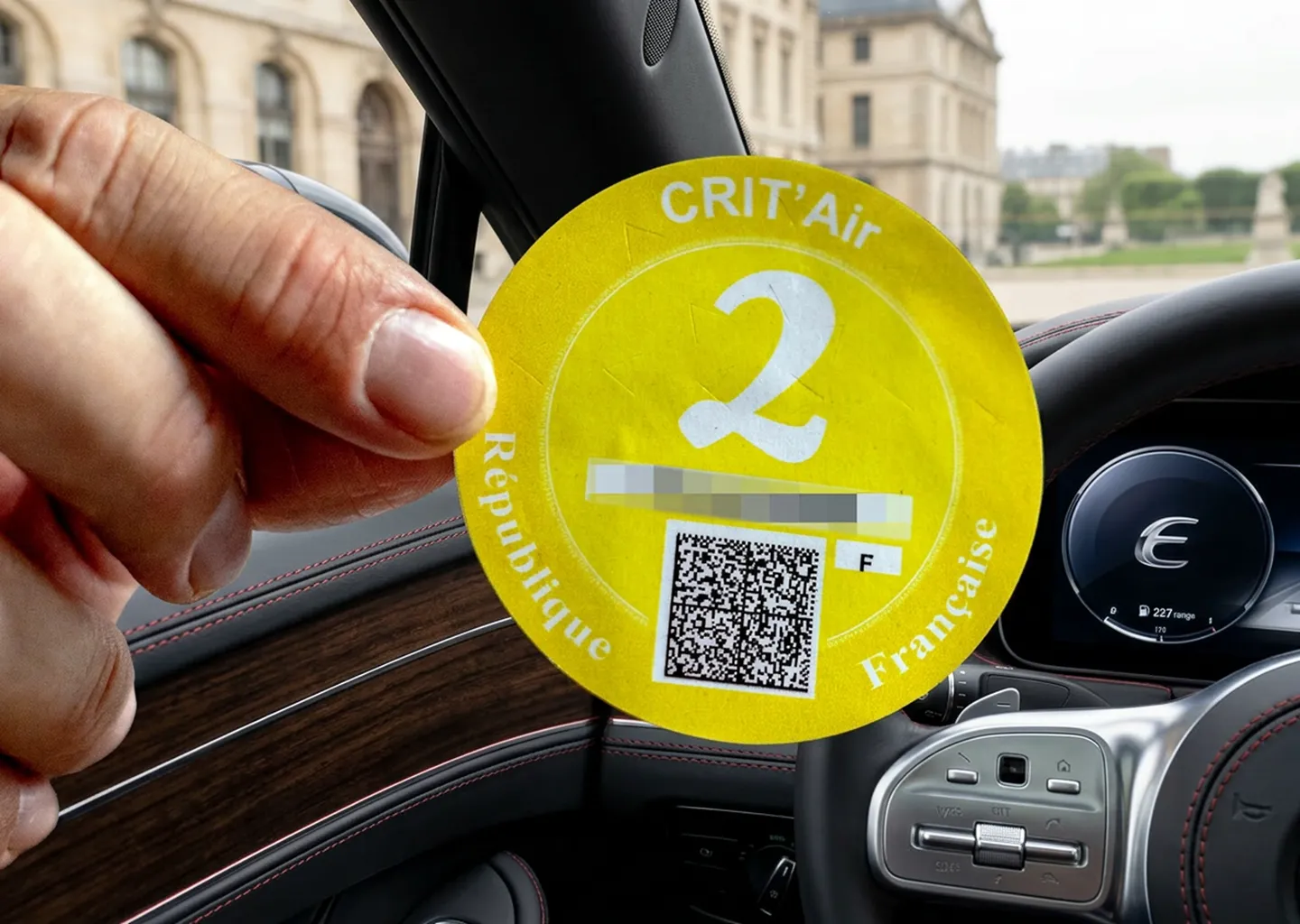 Main apposant une vignette Crit'Air sur le pare-brise d'une voiture